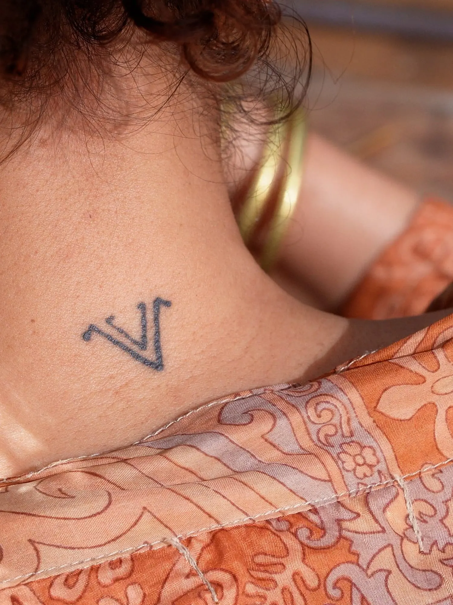 Het V-monogram van La Vie Nomade als tattoo in de nek