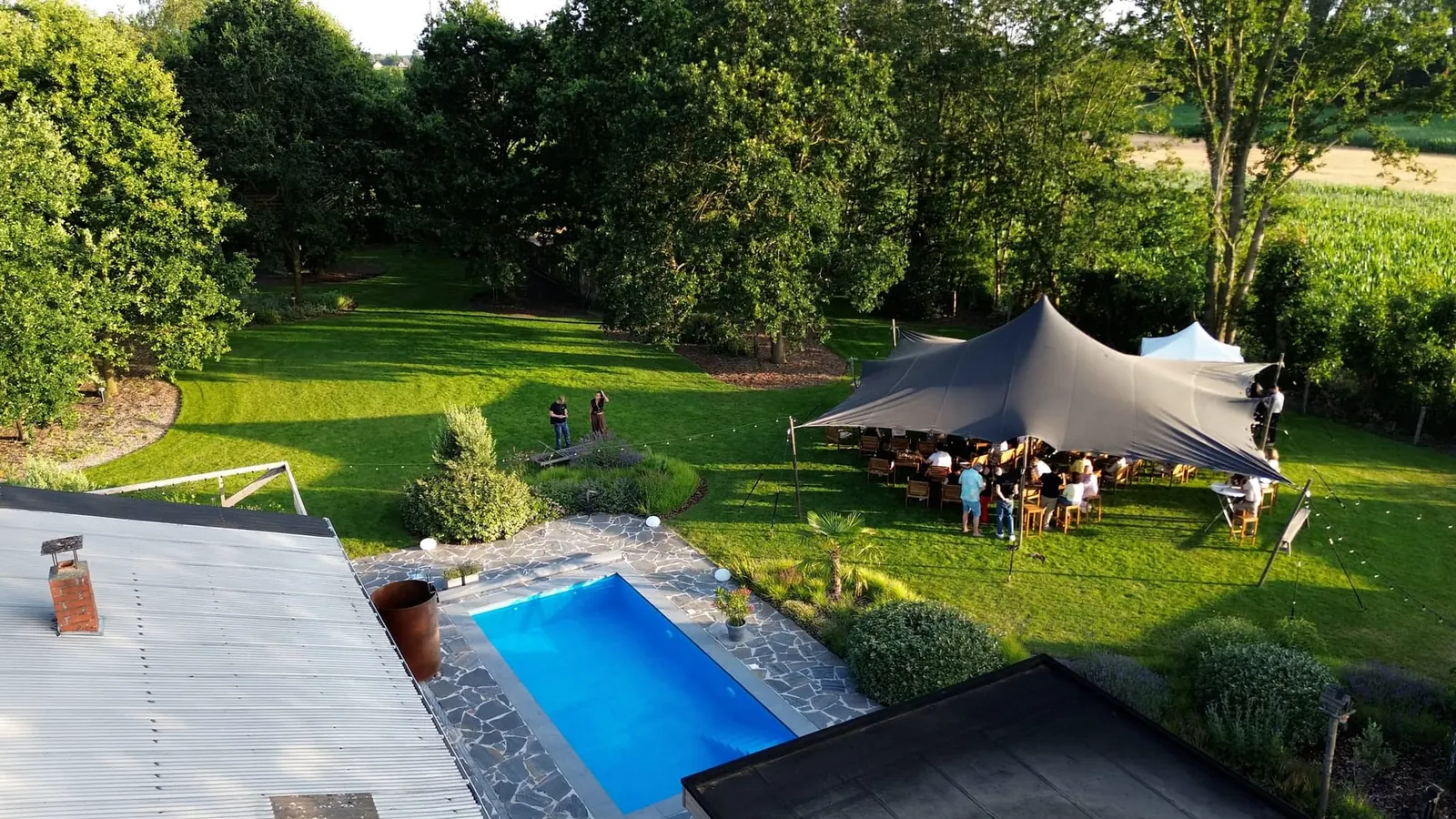 Luchtbeeld van de tuin en het zwembad, met gasten onder een tent